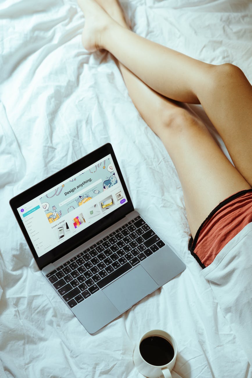 crop woman with laptop and coffee in bed at home