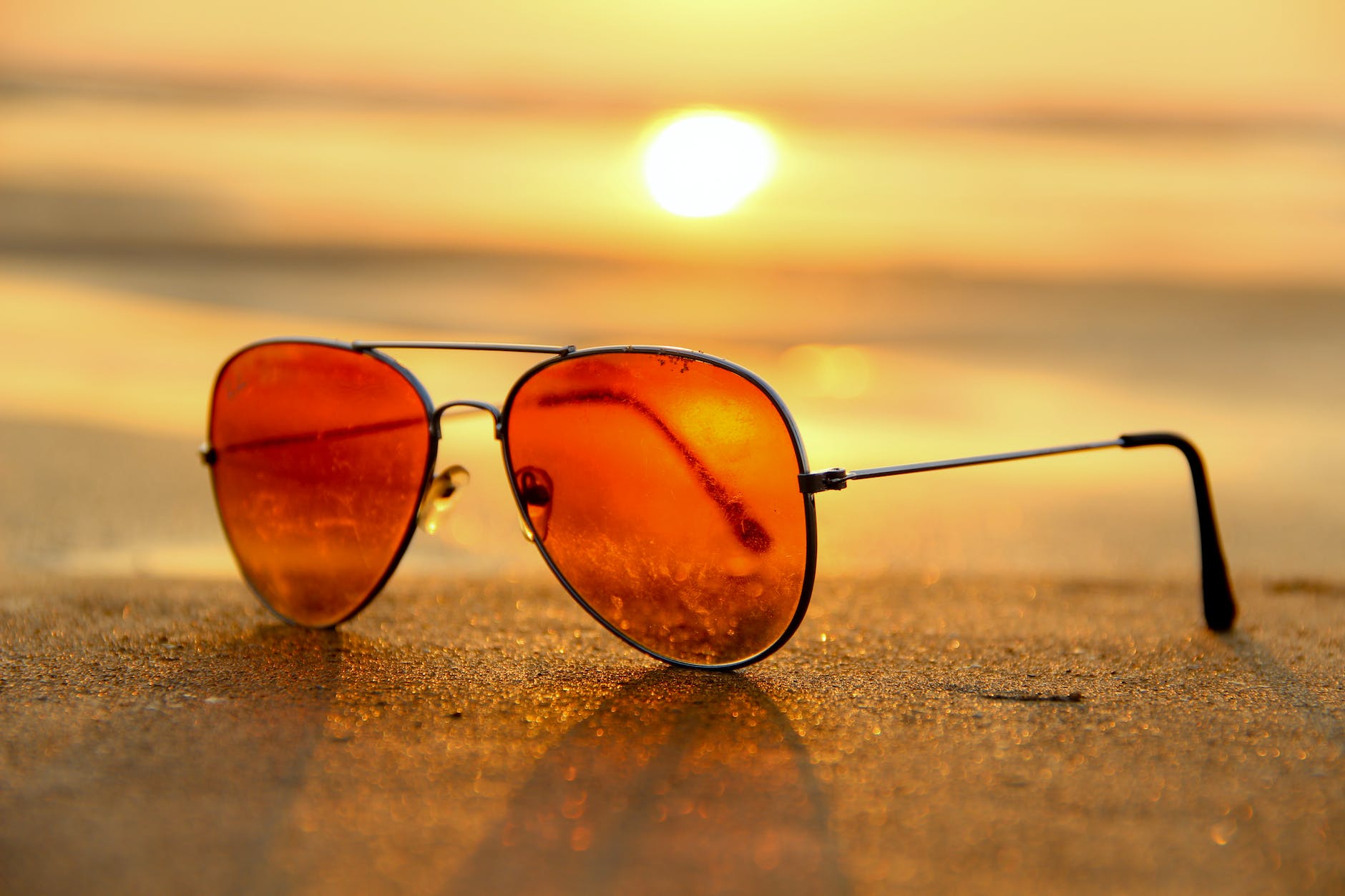 red lens sunglasses on sand near sea at sunset selective focus photography