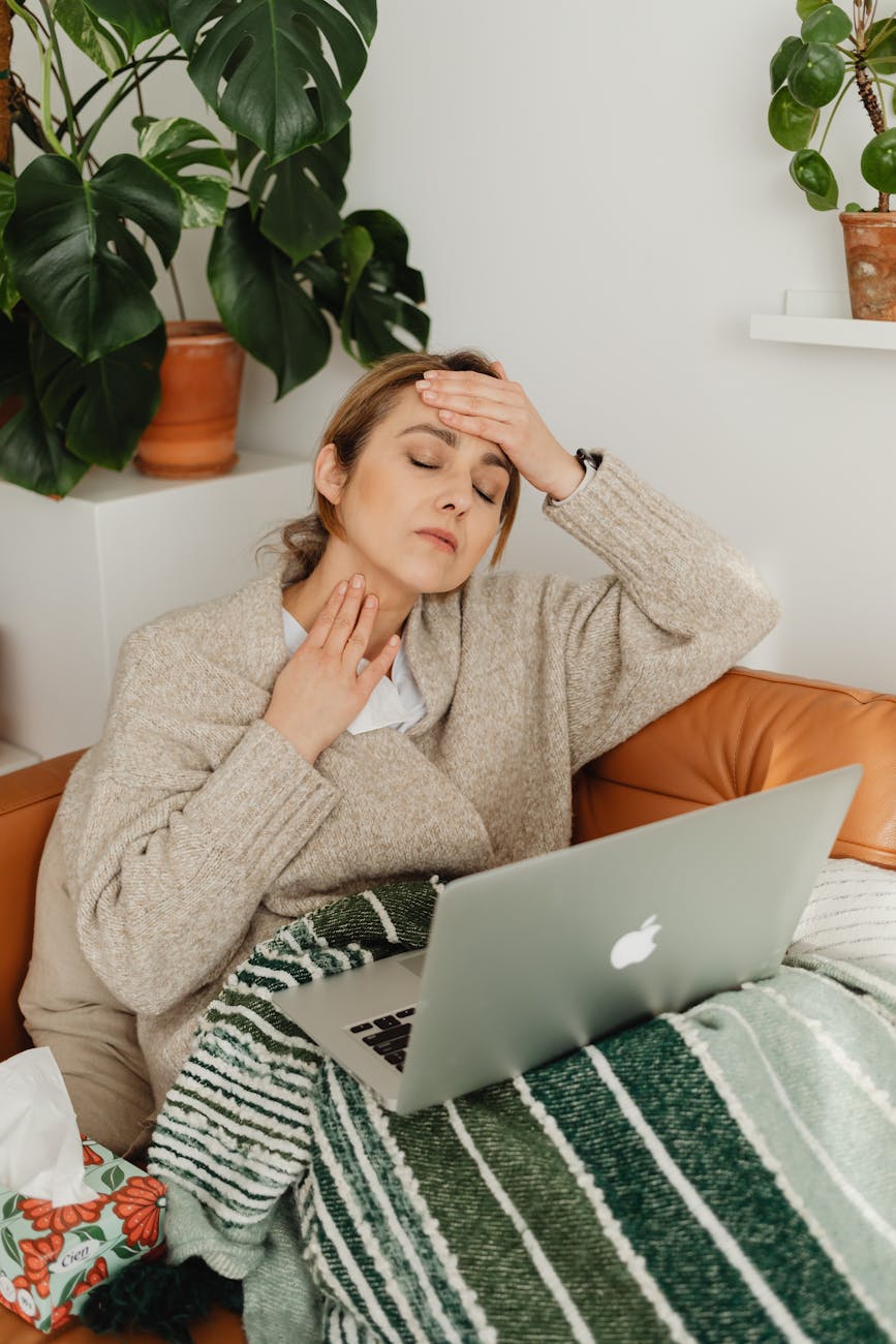 woman in brown sweater sitting on couch touching her head and neck