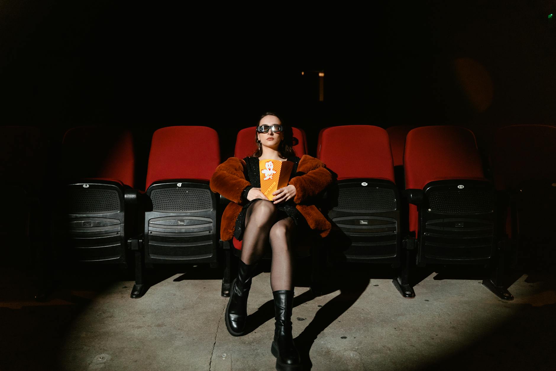 woman sitting inside a movie theater holding popcorn